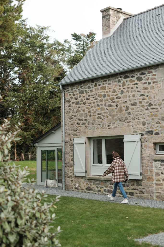 Une femme marche au pied d'une maison en pierres